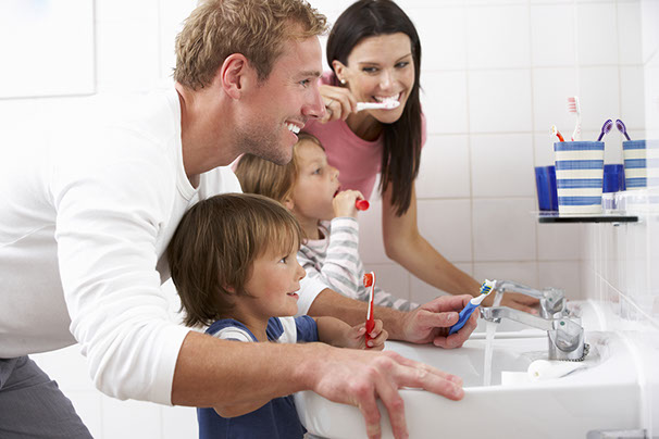 Photo of family brushing their teeth together in front of the bathroom sink and mirror.